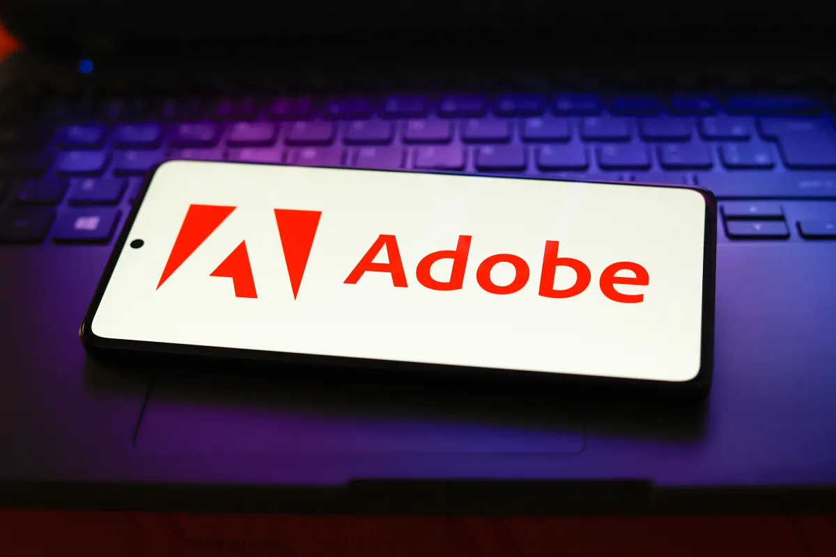 Smartphone displaying Adobe logo on a laptop keyboard, illuminated with purple light.
