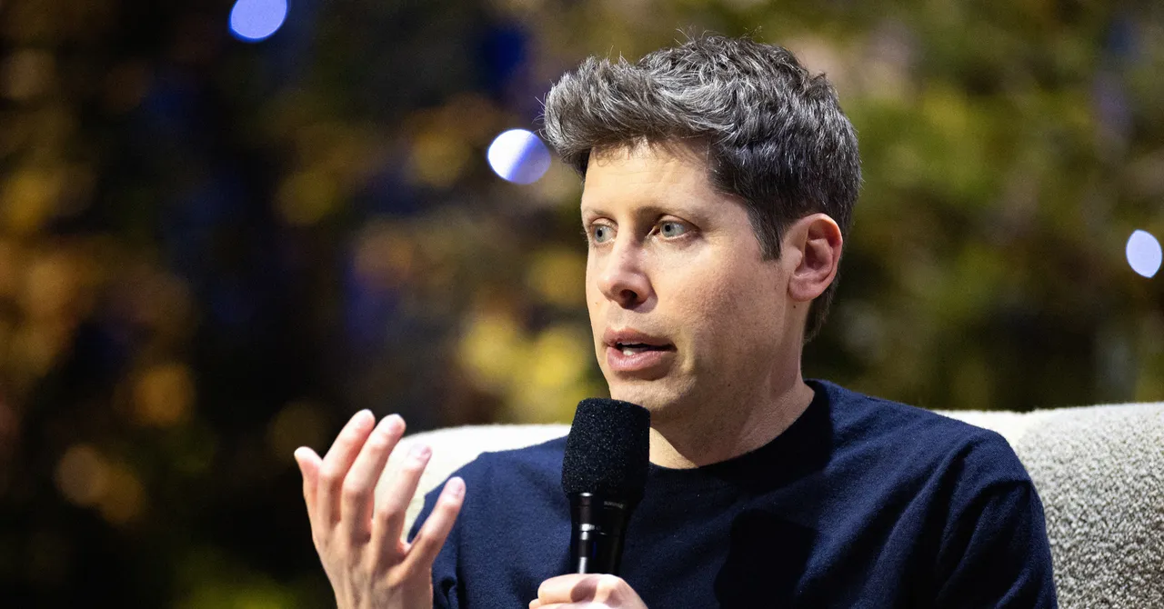 Person speaking into a microphone, gesturing with one hand, blurred background with lights.