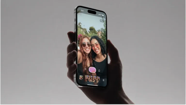 Hand holding a smartphone displaying a selfie of two smiling people with sunglasses, camera app interface visible