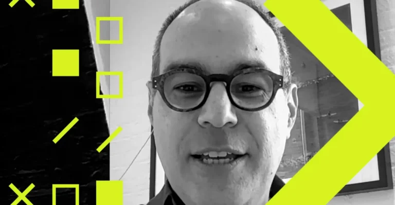 Man with glasses speaking, surrounded by yellow geometric shapes, black and white background.