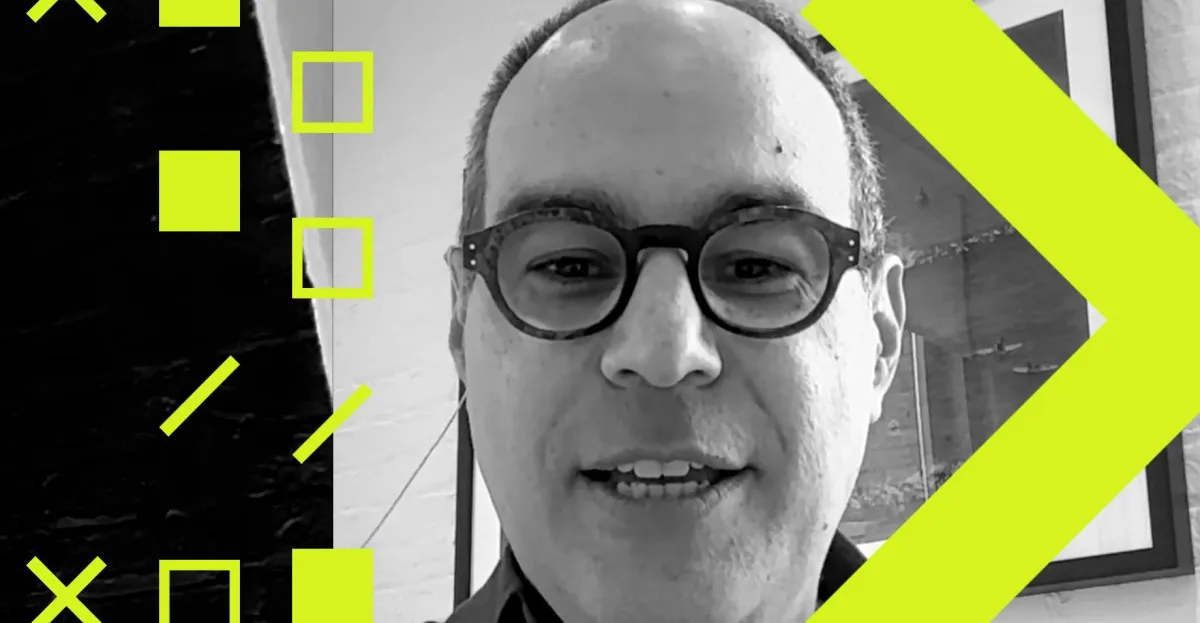 Man with glasses speaking, surrounded by yellow geometric shapes, black and white background.