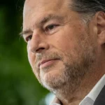 Man in a suit with a contemplative expression, blurred green background.