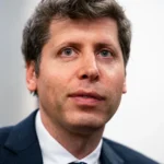 Man in a dark suit looking forward with a neutral expression against a plain background.