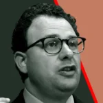 Man with glasses speaking, dark and red split background, close-up.