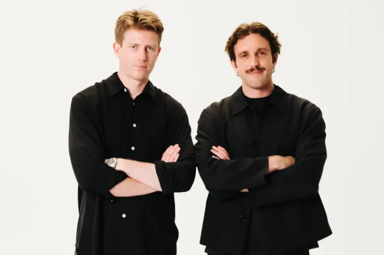 Two men in black shirts stand with arms crossed against a plain white background.