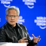 Man in a black jacket speaks onstage with microphones, blue backdrop reads "World Economic Forum".