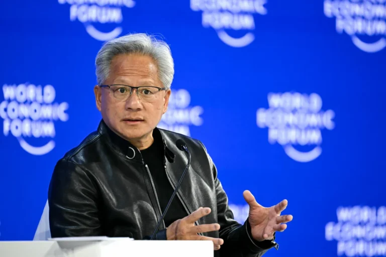Man in a black jacket speaks onstage with microphones, blue backdrop reads "World Economic Forum".