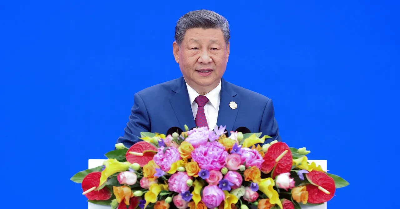 Man in a blue suit speaks at a podium adorned with colorful flowers against a blue background.