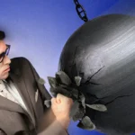 Man in a suit and glasses punches a large wrecking ball, causing cracks, against a blue background.