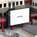 Large Meta sign displayed on a screen outside a modern building with red accents, a person walking nearby.