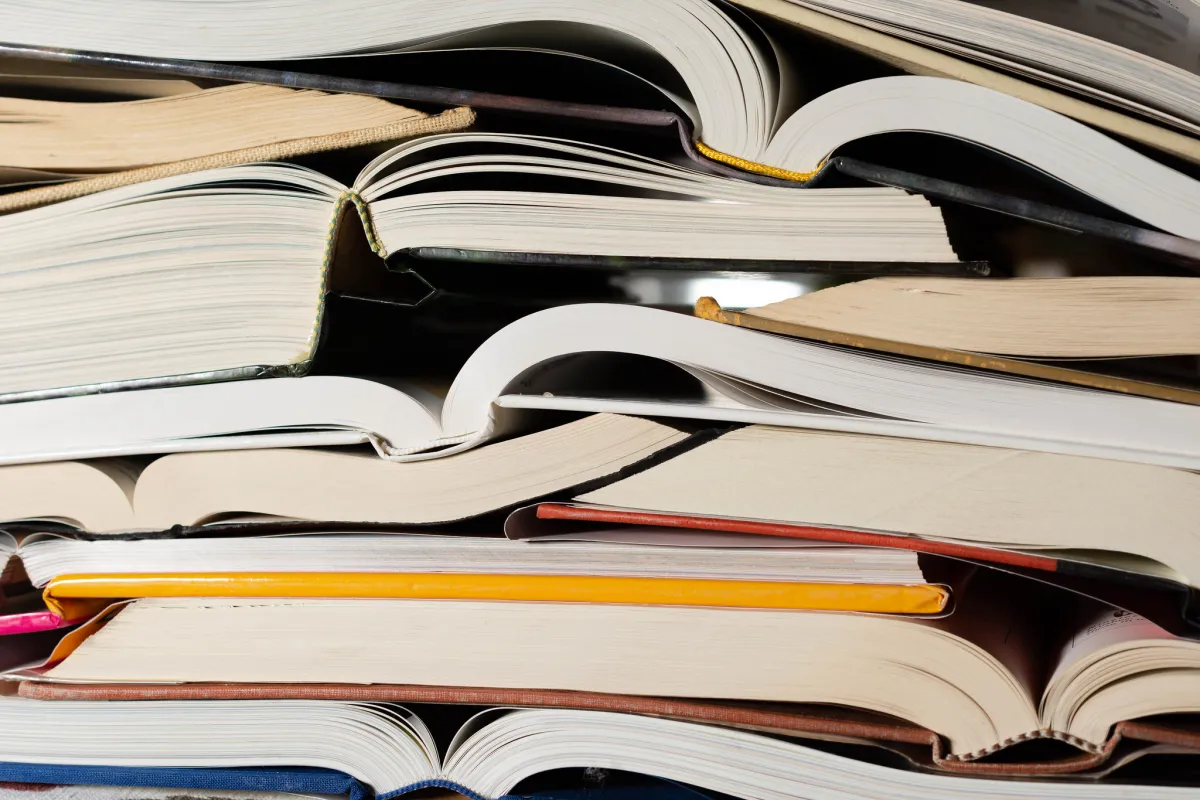Stack of open and closed books with visible spines and pages, some books overlapping, a yellow pencil among them.