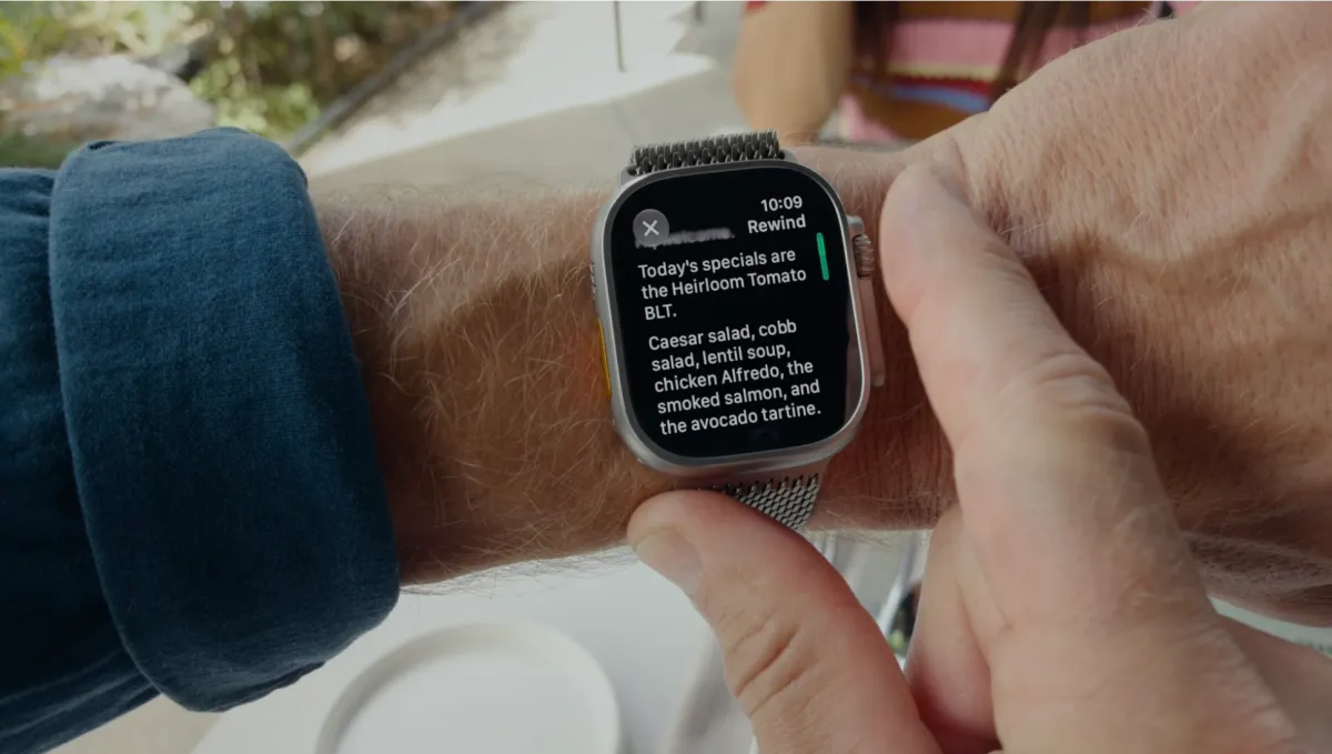 Person interacting with a smartwatch displaying menu specials, including heirloom tomato BLT and Caesar salad.