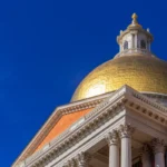 Massachusetts State House with a golden dome and blue sky background.