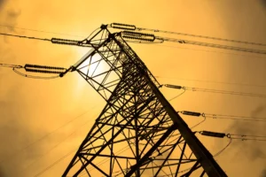 Electric transmission tower under a golden sky with visible power lines and insulators, sun partially obscured.
