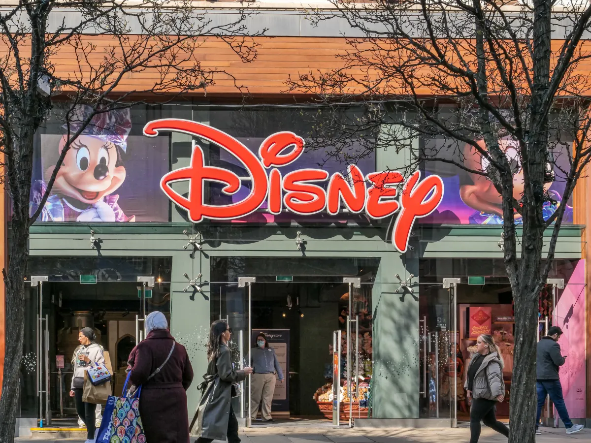 People walking in front of a disney store with large logo and character images on the facade
