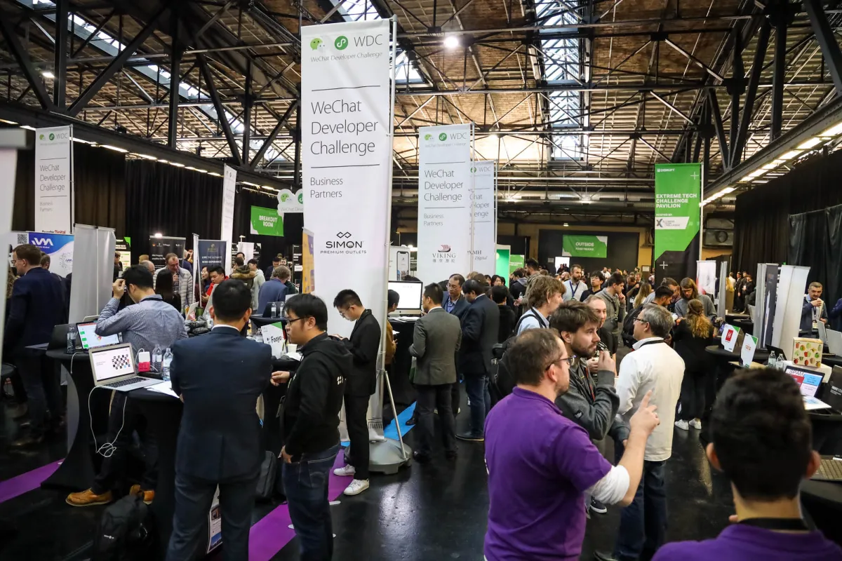 Crowded tech conference floor with people networking and banners for WeChat Developer Challenge and Extreme Tech Pavilion.