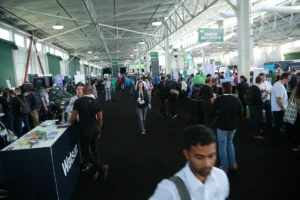 Crowded expo hall with booths and attendees, banners for "Startup Battlefield" visible, people engaged in conversations.