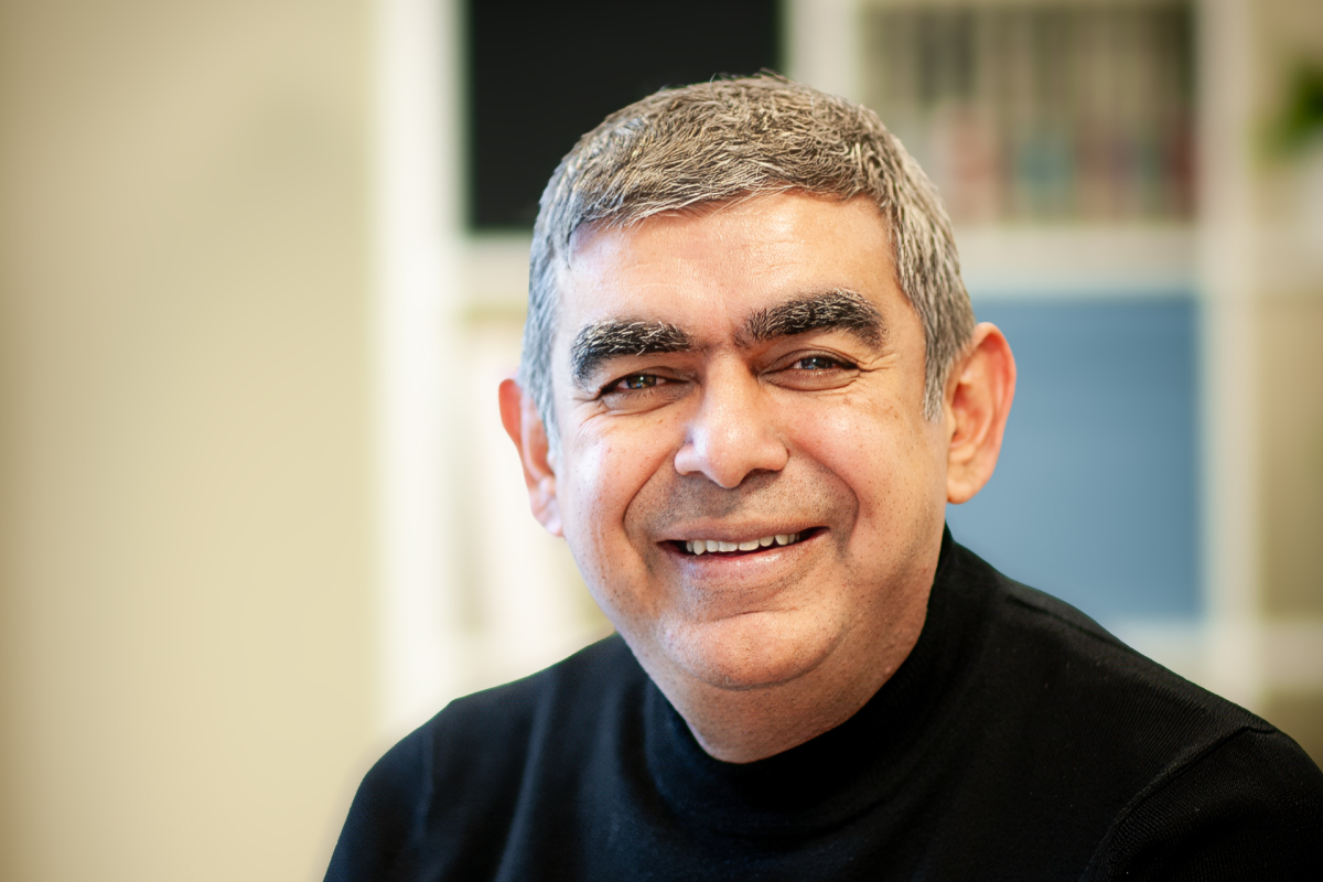 Smiling man with short gray hair and a black shirt in a blurred office setting.