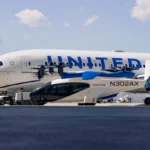 Small aircraft N302AX parked in front of a large United airplane on an airport tarmac under a partly cloudy sky.