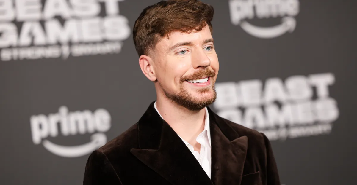 Smiling man in a dark suit at an event, with blurred "prime" and "beast games" logos in the background.