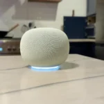 Smart speaker with a glowing blue base on a kitchen counter, stove and cabinets in the background.