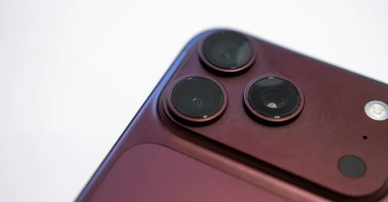Close-up of a burgundy smartphone's rear camera setup with three lenses and a flash on a light background.