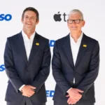 Two men in suits smiling, standing in front of a backdrop with Apple TV logo and "Ted Lasso" text.