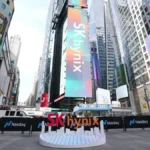 SK Hynix and Nasdaq logos displayed on digital billboards in a cityscape with skyscrapers and a small stage setup.