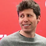 Person smiling in front of a red background with partial white text visible.