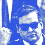 Man in sunglasses, wearing a suit, with a thumb gesture. Blue and green gradient overlay.