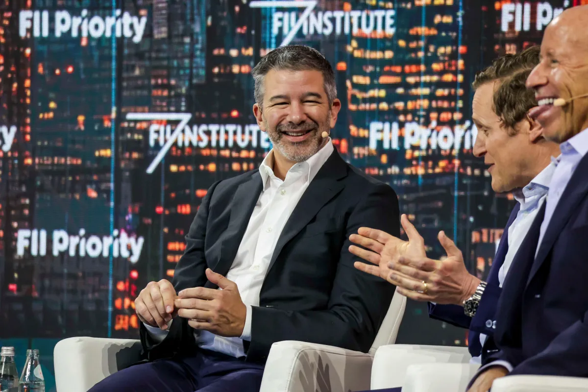 Three men in suits engaged in a lively discussion on stage with "FII Priority" displayed in the background.
