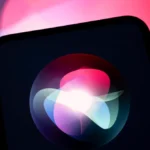 Smartphone screen displaying a colorful Siri logo, set against a blurred pink and blue background.