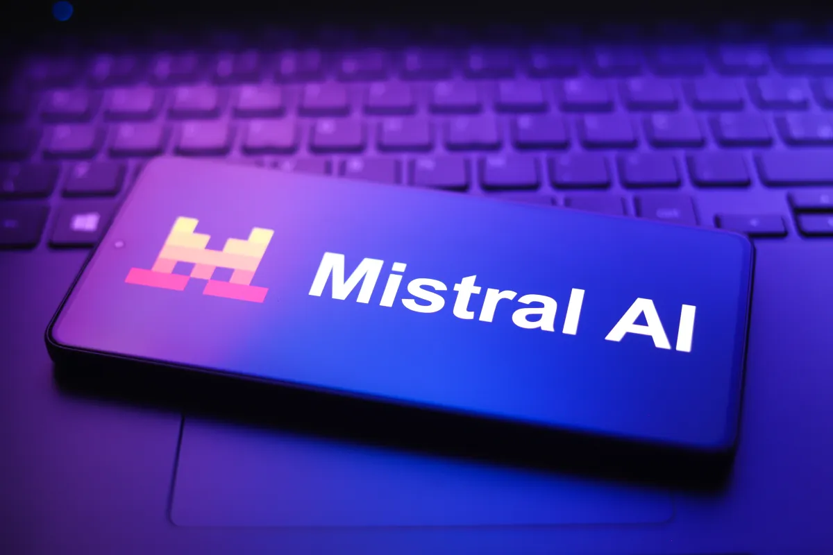 Smartphone displaying "Mistral AI" logo, resting on a laptop keyboard under purple lighting.