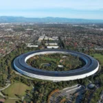 Aerial view of Apple's circular headquarters surrounded by greenery and a sprawling urban landscape in the background.