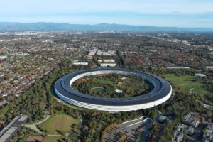 Aerial view of Apple's circular headquarters surrounded by greenery and a sprawling urban landscape in the background.