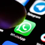 Close-up of a finger hovering over the WhatsApp app icon on a smartphone screen, surrounded by other app icons.