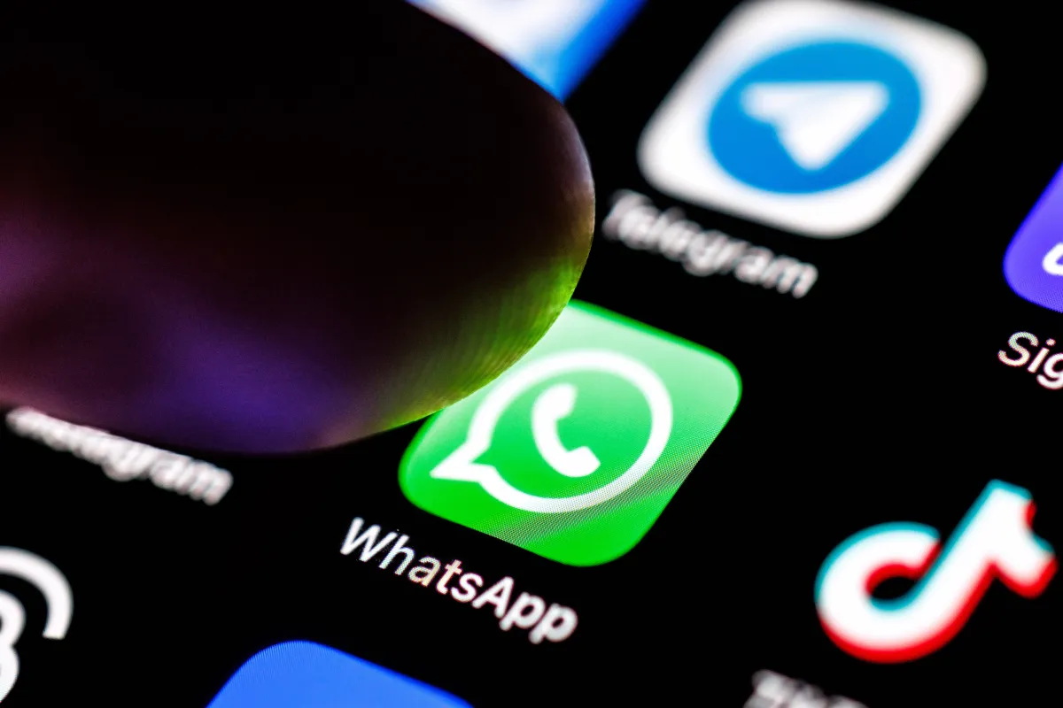 Close-up of a finger hovering over the WhatsApp app icon on a smartphone screen, surrounded by other app icons.