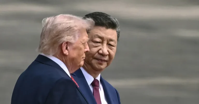 Two men in suits walking closely together, one with light hair and the other with dark hair, in an outdoor setting.