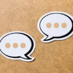 Two white speech bubble icons with ellipses on a wooden background.