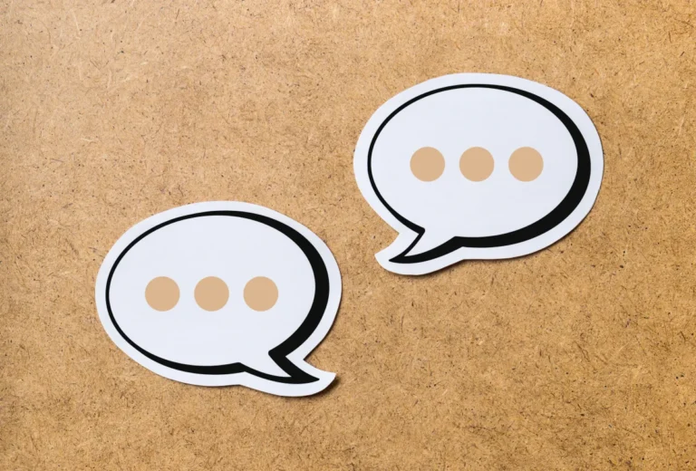 Two white speech bubble icons with ellipses on a wooden background.