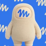 Furry beige character with a blue "M" on its face, set against a blue background with repeating "M" pattern.