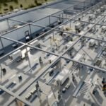 Interior of a large industrial facility with modular units, machinery, and overhead cranes, viewed from above.