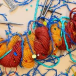Colorful yarn entangled with blue threads, beads, and sewing tools on a beige surface, resembling a complex network.
