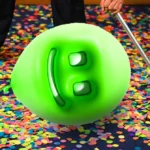 Green smiley balloon on confetti-covered floor, person sweeping with a broom.