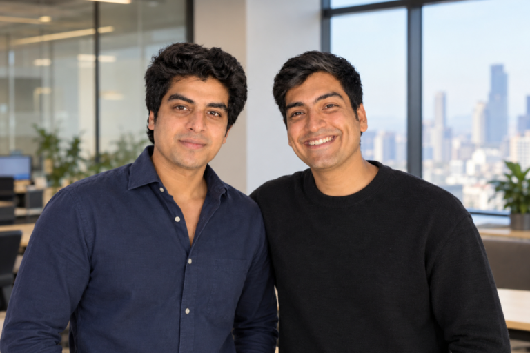 Two men smiling in a modern office with large windows and cityscape background.