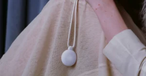 White AI pendant on a beige fabric, worn around the neck, close-up view.