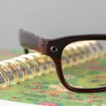 Close-up of dark-framed smart glasses with a camera, resting on a floral spiral notebook.