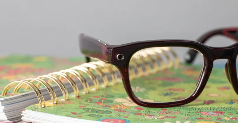 Close-up of dark-framed smart glasses with a camera, resting on a floral spiral notebook.