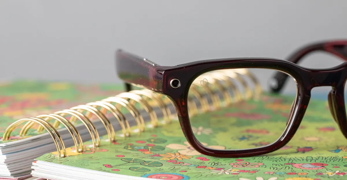 Close-up of dark-framed smart glasses with a camera, resting on a floral spiral notebook.