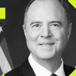 Smiling man in a suit with abstract yellow shapes and partial flag in the background.